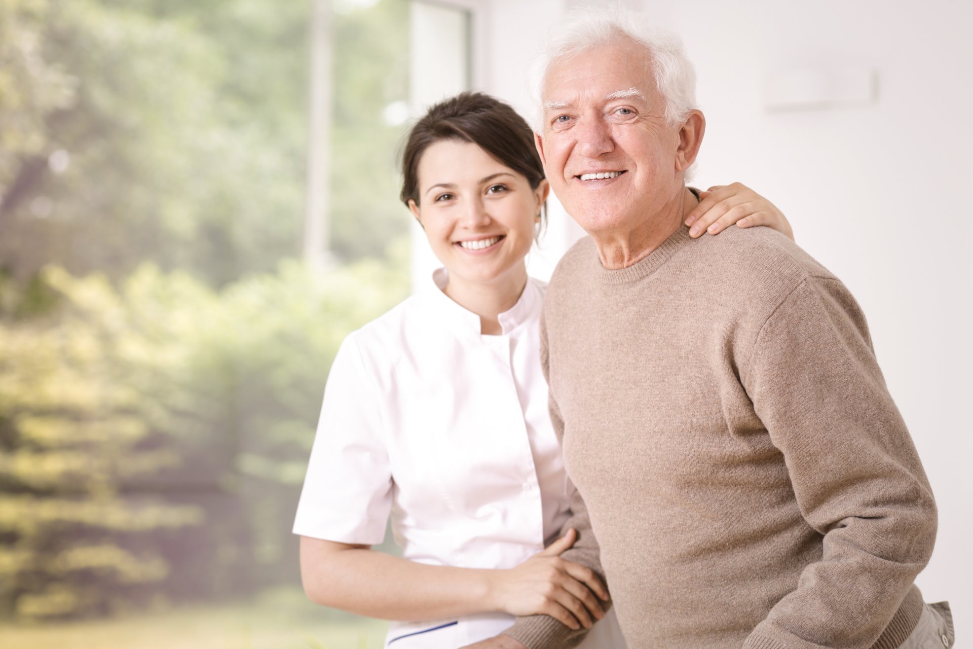 Una caregiver accompagna con un abbraccio un anziano sorridente